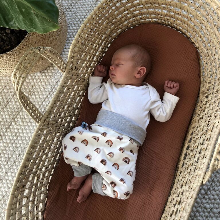 Ein schlafendes Baby liegt in einem Körbchen. Es trägt eine Mitwachshose von Tulipanelli.